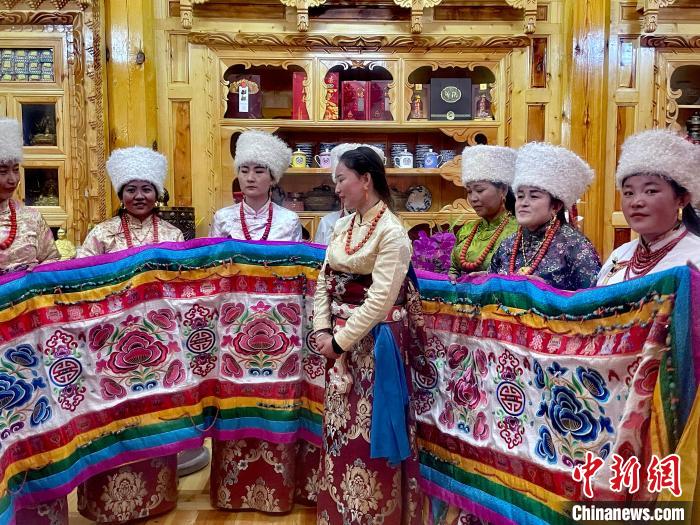 圖為女性展示村民自發(fā)繡制的“百米五彩哈達(dá)”。　李玉峰 攝